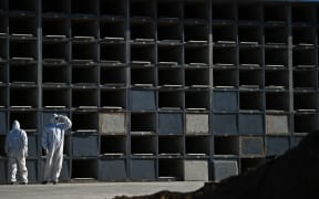 Cemetery workers wearing protective clothing wait by grave cubicles to perform a funeral for a Covid-19 victim in Rio de Janeiro, Brazil