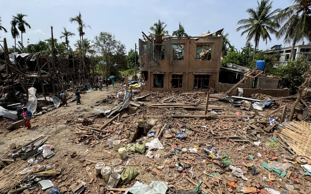 People walk past destroyed buildings following Myanmar military airstrikes in Kyauktaw town in Myanmar's western Rakhine State on May 15, 2025. (Photo by AFP)