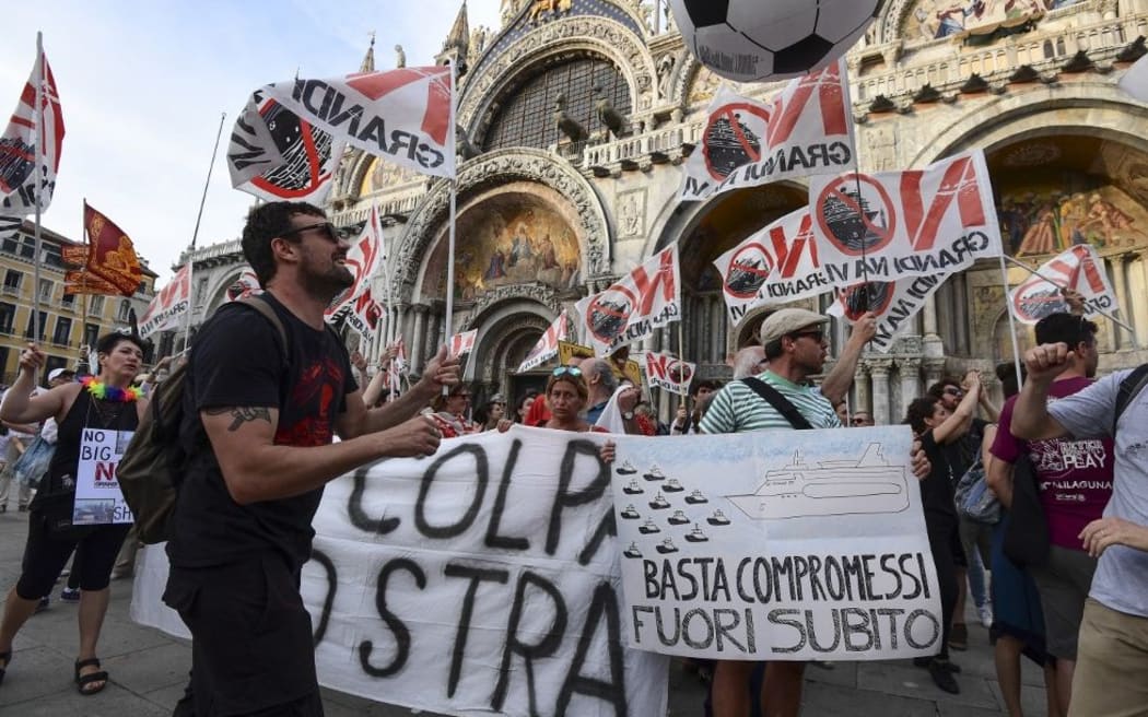 People hold flags and banners as they arrive in San Marco square in Venice at the end of a demonstration called by the No Great Ships movement against big cruise ships sailing into the Venice lagoon on June 8, 2019.