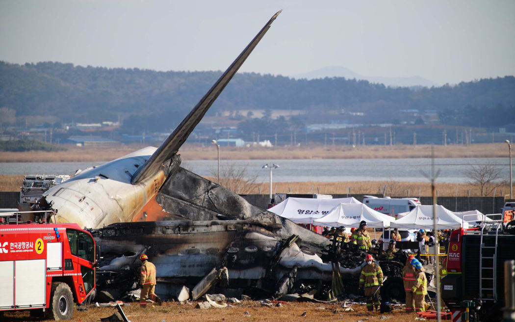 Rescue personnel work near the tail section of a Jeju Air Boeing 737-800 series aircraft after the plane crashed and burst into flames at Muan International Airport in South Jeolla Province, some 288 kilometres southwest of Seoul on December 29, 2024. - A Jeju Air plane carrying 181 people from Bangkok to South Korea crashed on arrival December 29, killing at least 85, emergency services said, with a bird strike and adverse weather conditions cited as likely causes. (Photo by YONHAP / AFP) / - South Korea OUT / NO USE AFTER JANUARY 8, 2025 05:04:26 GMT - - SOUTH KOREA OUT / NO ARCHIVES - RESTRICTED TO SUBSCRIPTION USE
