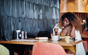 A woman sitting at a restaurant and eating a salad.