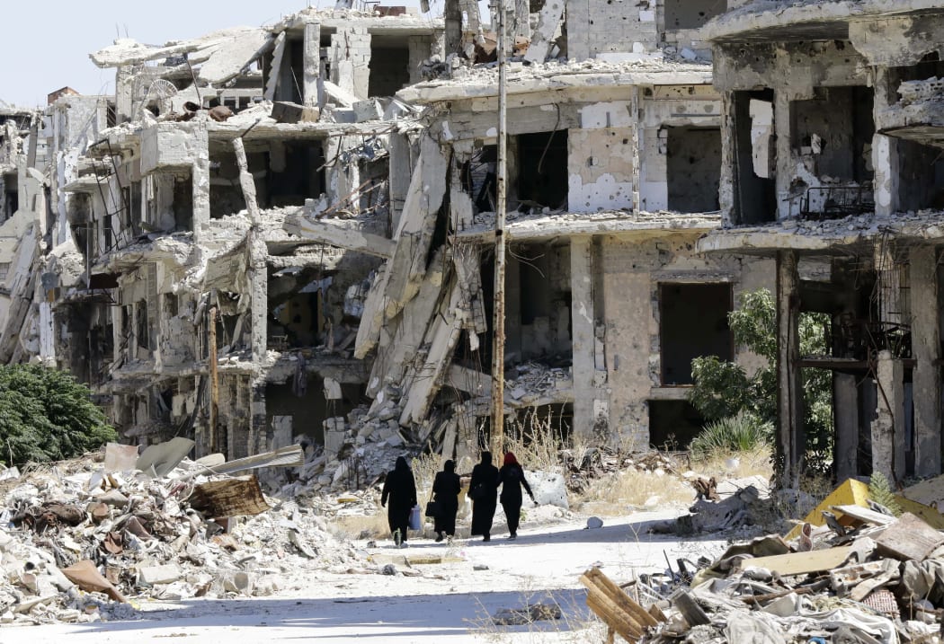 This file photo taken on September 19, 2016 shows Syrian women walking in between destroyed buildings in the government-held Jouret al-Shiah neighbourhood of the central Syrian city of Homs.
