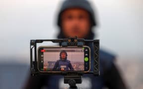 A Palestinian journalist uses the mobile phone to broadcast live in Rafah on the southern Gaza Strip on December 27, 2023, amid continuing battles between Israel and the Palestinian militant group Hamas. Power cuts have become a fact of life in war-torn Gaza. But thanks to embedded SIM cards, Palestinians can still access the internet and stay in touch with loved ones abroad. (Photo by SAID KHATIB / AFP)