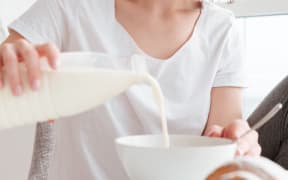Portrait of a smiling young woman pouring milk into the bowl while having breakfast at the kitchen