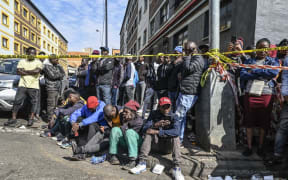 Residents, relatives of victims and members of the public gather behind a police tape at the site of a burned apartment block in Johannesburg on 1 September, 2023.