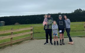 The Stockers - Poppy, Brad, Robbie, Dean, and Ellie, stand at the entrance to where their home would be by now, if not for an ongoing hold up around wastewater consents.