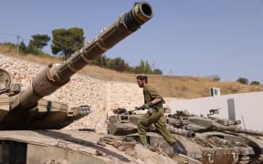 An Israeli soldier walks on a Merkava tank at a position in an undisclosed location on the border with Lebanon on October 22, 2023. Lebanon's Iran-backed Hezbollah and allied Palestinian factions have traded cross-border fire with Israel for days, after Hamas gunmen attacked communities in southern Israel on October 7. (Photo by Jalaa MAREY / AFP)