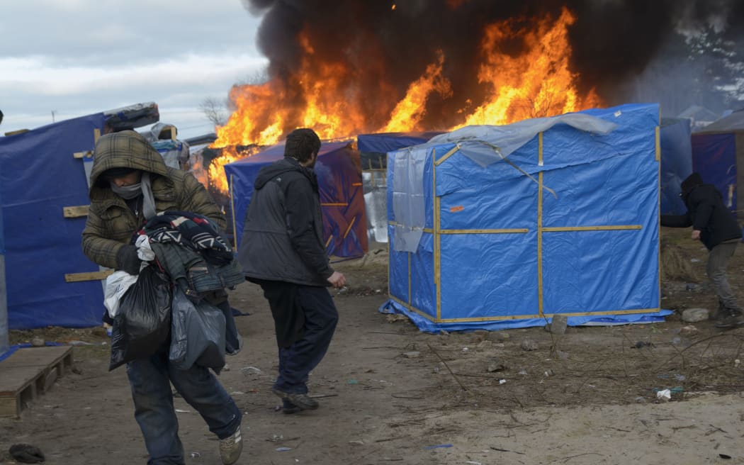 A migrant looks on as a hut in the camp burns.