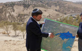 Israeli far-right Finance Minister Bezalel Smotrich holds a map of an area near the settlement of Maale Adumim, a land corridor known as E1, outside Jerusalem in the occupied West Bank, on August 14, 2025, after a press conference at the site. Far-right ministers have in recent months openly called for Israel's annexation of the territory. Plans exist to build 4,000 housing units, schools, health clinics and a country club on E1 between Maale Adumim and Jerusalem. (Photo by Menahem Kahana / AFP)