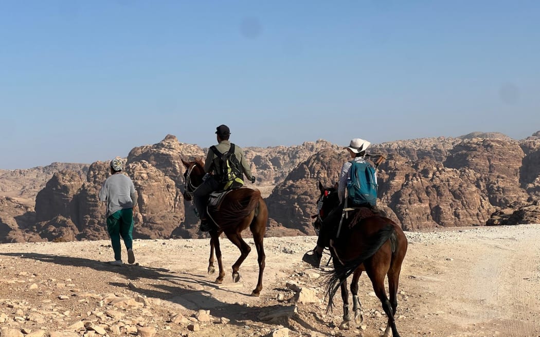 Two horses carry tourists over the desert landscape of Jordan