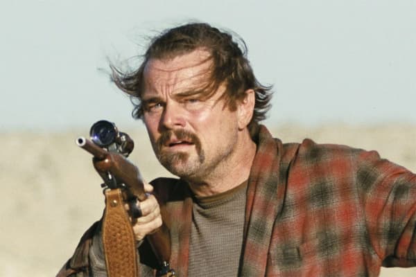 Leonardo DiCaprio holds a gun, his hair is blown around and his face looks wild.
