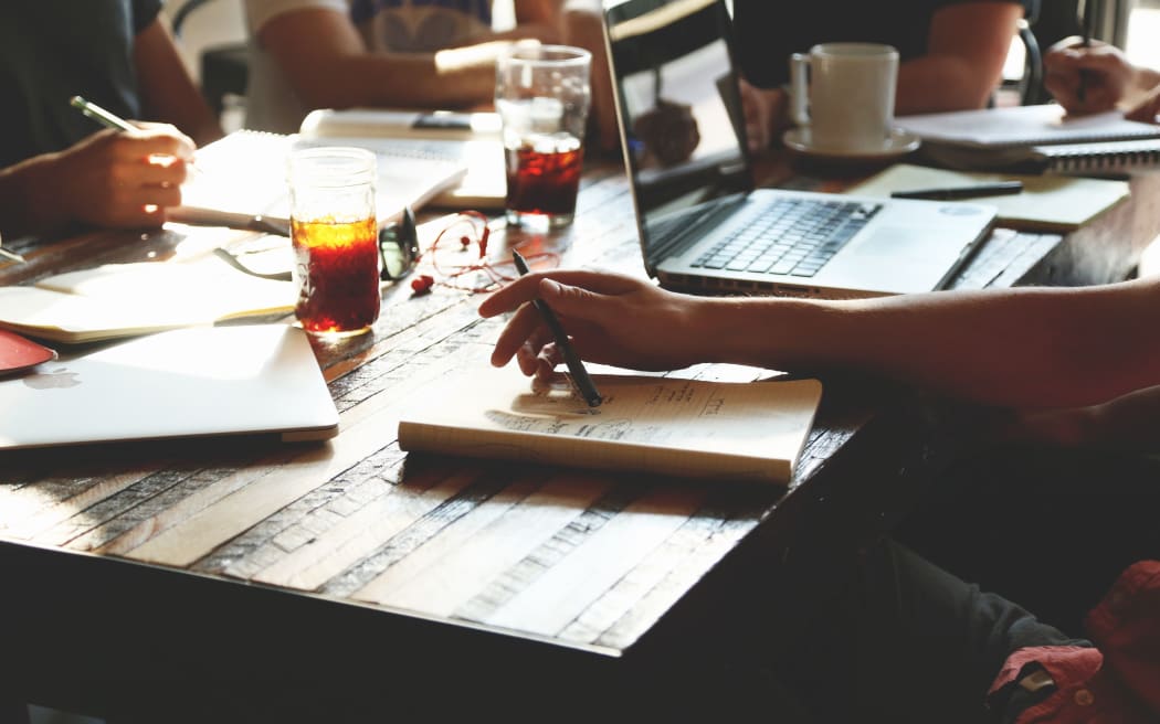 people studying meeting at a table with books, coffee, drink, pen, laptop.