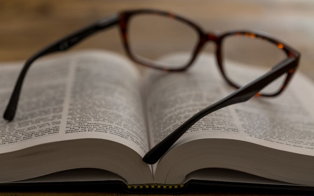 Open book with glasses on brown wooden desk, closeup.