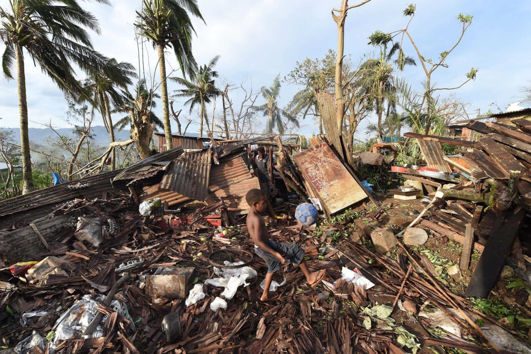 A young boy kicking a ball as his father searches through the ruins of their family home in Vanuatu's capital Port Vila.