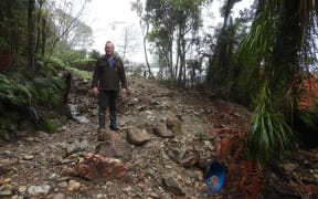 Northern Buller Museum Trust chair Derek Lord points to the culvert which blocked in February, diverting the stream to the museum buildings rear.