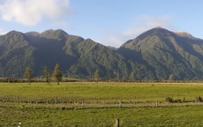 LDR image: A view of the Taramakau River Valley looking from Murray Stewart's Turiwhate farm towards Taramakau Settlement, at the base of the Hōhono Range in the distance. The land is modified from earlier milling, then pastoral farming for the past 100 years. Seven farms at Taramakau Settlement have been captured by an Outstanding Natural Landscape designation in the proposed Te Tai o Poutini Plan. Hōhuno (correct spelling Ōhonu) separates the Taramakau River valley from nearby Lake Brunner (Kōtukuwhakaoka).