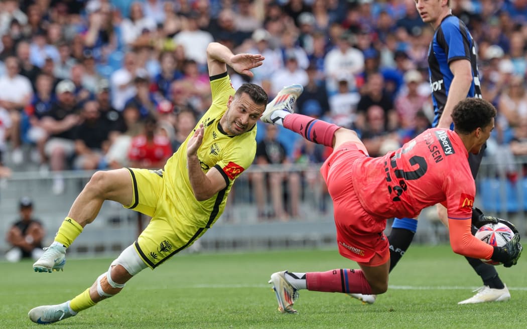 Auckland FC's Alex Paulsen takes a battering from Wellington Phoenix's Kosta Barbarouses.