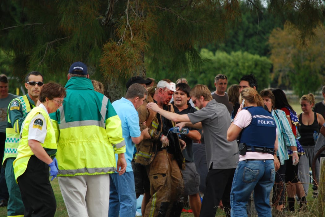 Tamahere people and emergency service people attending to a burnt fireman on the Tamahere School grounds.
