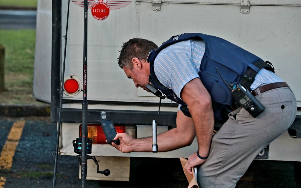 A police officer taking a photograph of a fishing rod that snagged a body wrapped in rubbish bags from the water at Gulf Harbour in Auckland on 12 March, 2024.