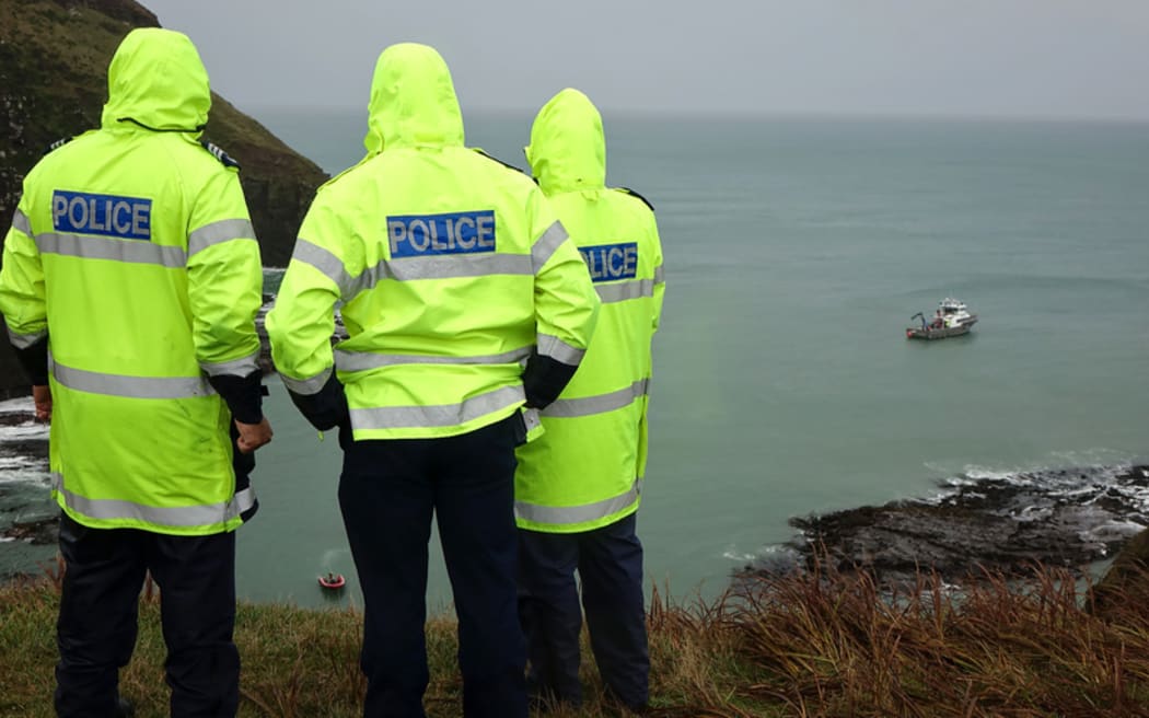 Police survey the recovery operation from the top of the cliff..