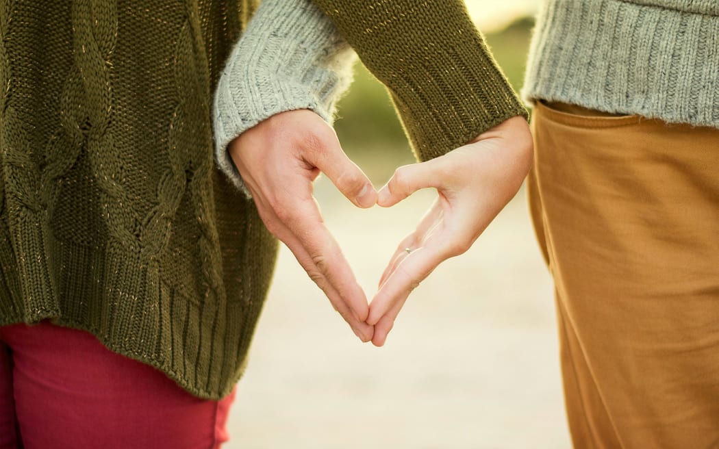 Couple linking hands to form a heart shape.