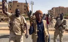 In this image grab taken from handout video footage released by the Sudanese paramilitary Rapid Support Forces (RSF) on 23 April 2023, fighters wave assault rifles as they cross a street in the East Nile district of greater Khartoum.