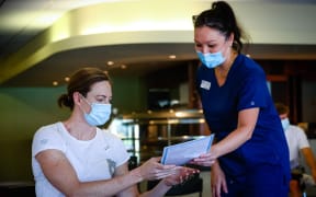 Three time Olympian Australian swimmer Cate Campbell (L) receives a fact sheet  on 10 May 2021, upon receiving the Pfizer/BioNTech vaccination against Covid-19 after the Australian Olympic Committee began their rollout of vaccinations for members of the Olympic team ahead of the the games in Tokyo.