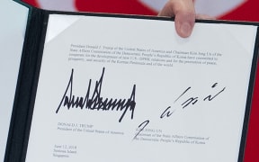 The signatures of US President Donald Trump (L) and North Korea's leader Kim Jong Un (R) are seen on a document held up by Trump following a signing ceremony during their historic US-North Korea summit