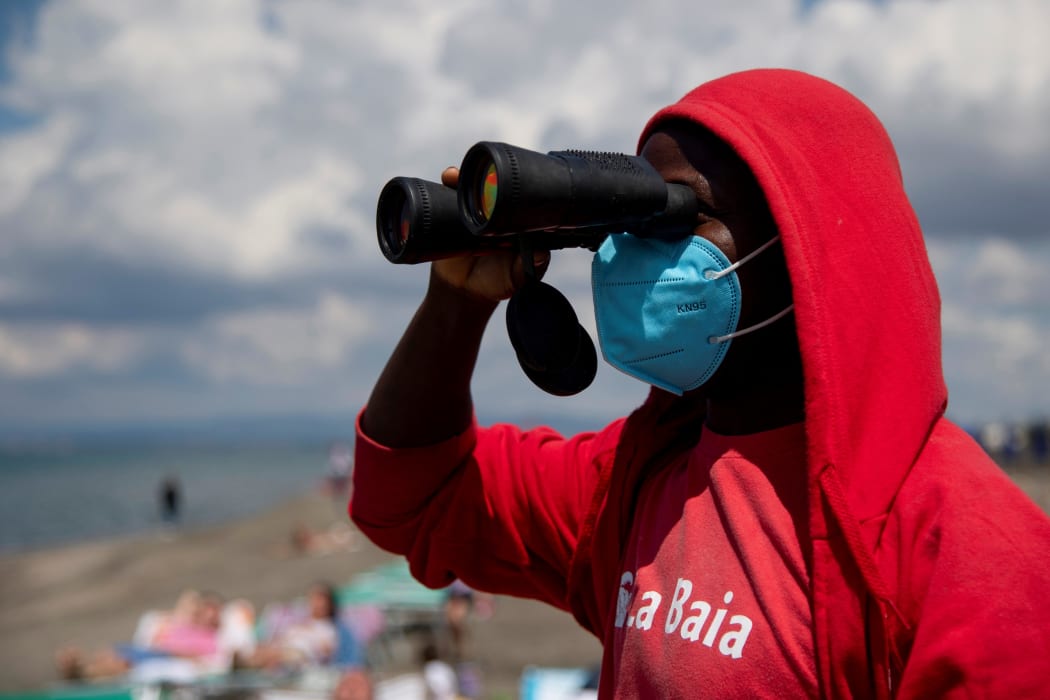 A lifeguard wearing a protective mask looks through his binoculars at a beach in Rome.
