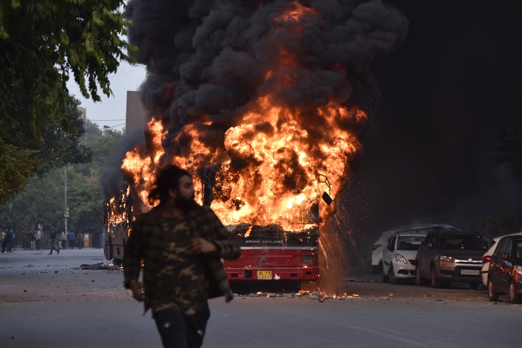 A man walks on a street as a bus is on fire following a demonstration against the Indian government's Citizenship Amendment Bill.