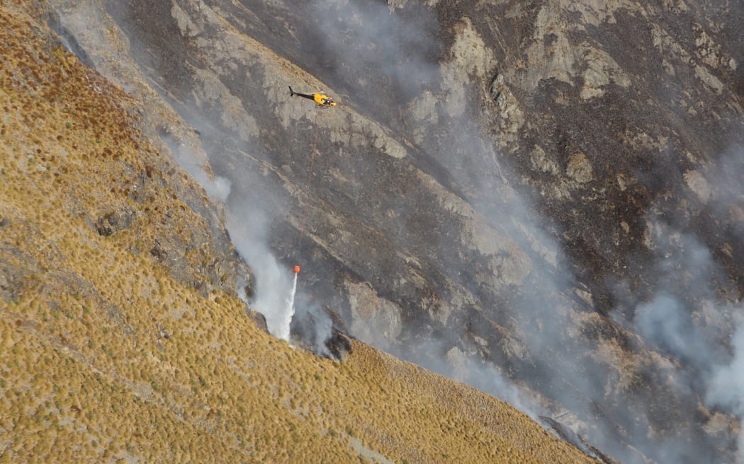 One of six helicopters working to contain the fire burning in steep terrain on Mt Creighton.