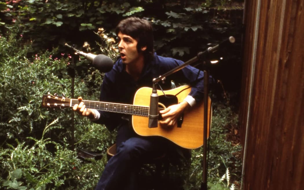 Paul McCartney playing his guitar in a garden