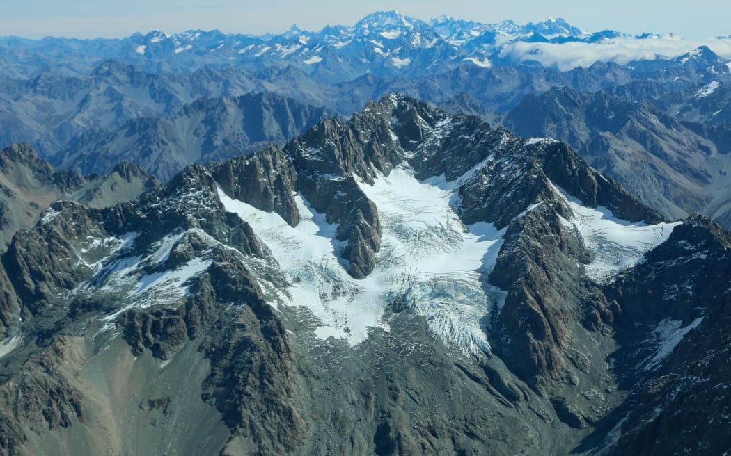 An aerial view of rocky mountains with snow and ice beneath a hazy sky.