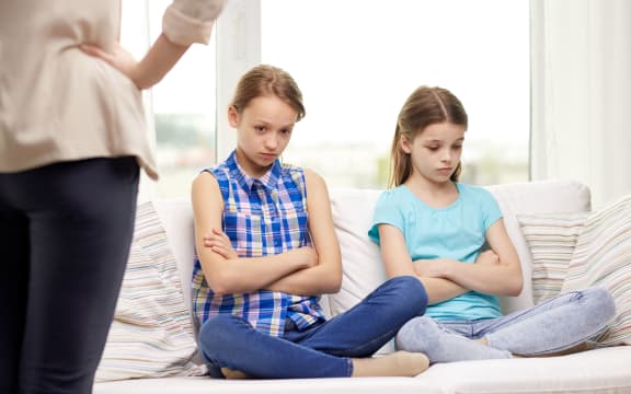 A photo of two girls sitting on the couch and looking chastened after a lecture from their mother