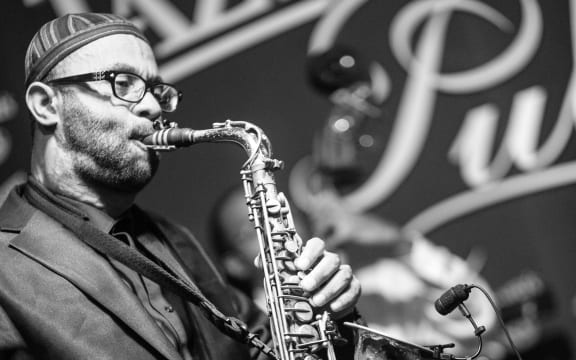 Kenny Garrett playing saxophone in front of a mural with the word "jazz" in it.