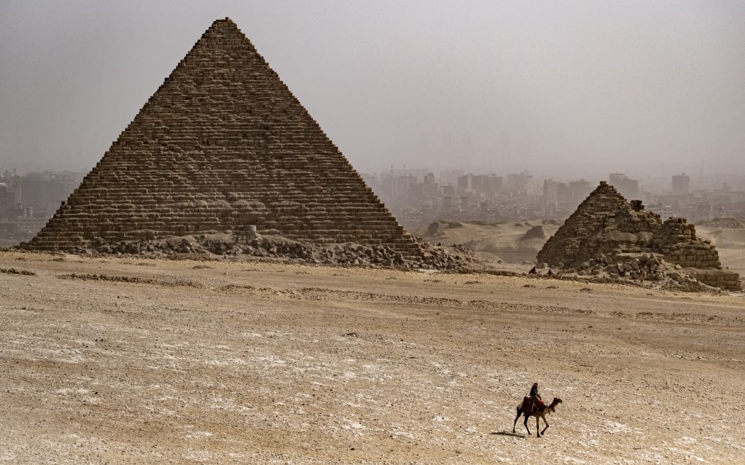 In this picture taken on February 6, 2023, a camel guide rides near the Pyramid of Menkaure (Menkheres) at the Giza Pyramids necropolis on the outskirts of the Egyptian capital. (Photo by Amir MAKAR / AFP)
