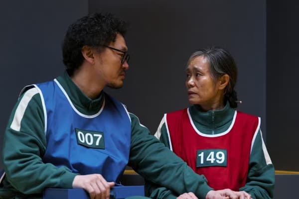 An Asian man and woman wearing colourful vests hold hands and look at each other with concern.