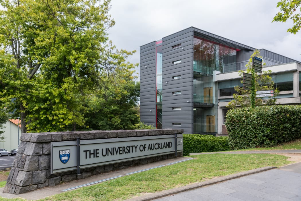 Auckland, New Zealand - March 1, 2017: Sign and logo of University of Auckland set near modern dark gray offices in green park like environment. Gray sky.