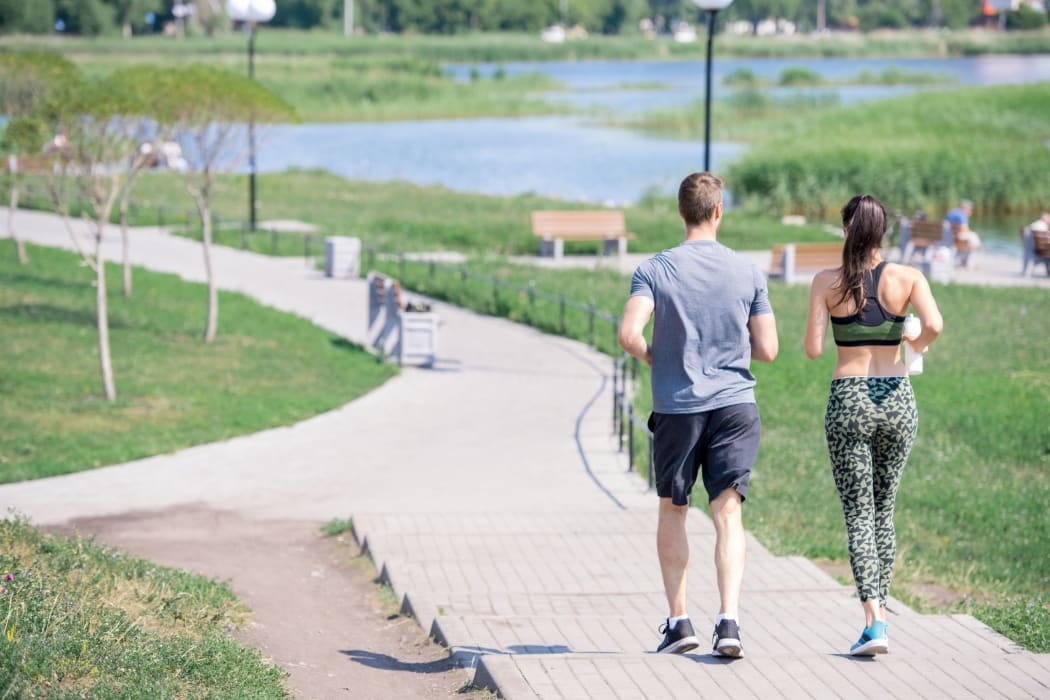 Back view portrait of modern young couple running together outdoors in city park, copy space