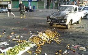 A picture released by the official Syrian Arab News Agency (SANA) shows a member of the Syrian security forces walking past a truck damaged in a suicide attack in Sweida.