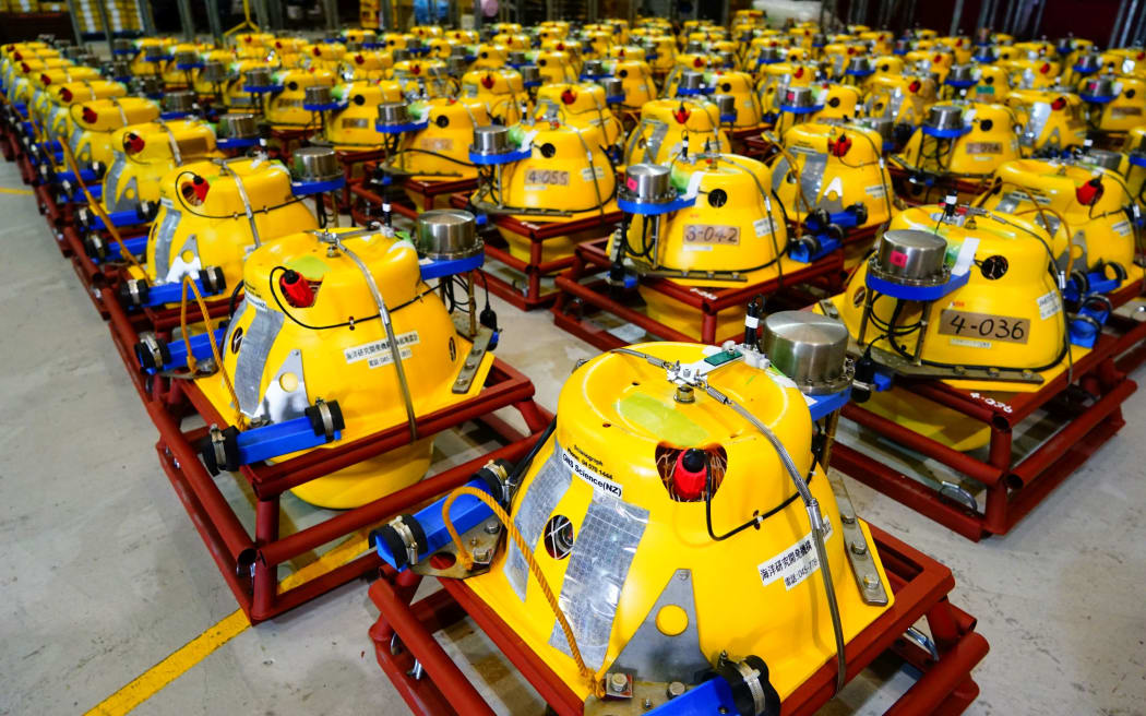 Approximately 50 large yellow devices, roughly spherical, with bright blue attachments, inside red square metal frames lined up.