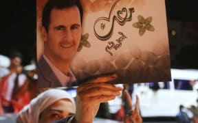 Woman holding poster of Bashar al-Assad.