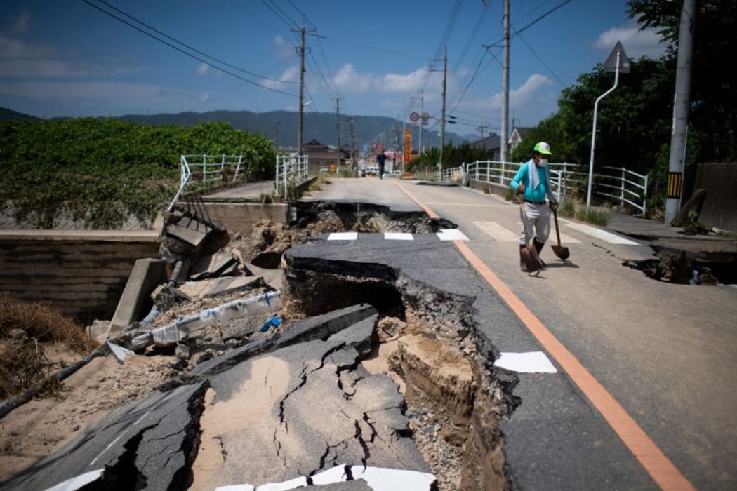 A man with a shovel walks on a damaged road in a flood hit area in Mabi, Okayama prefecture on 10 July, 2018.