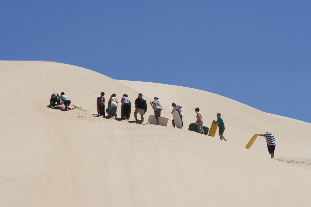 People waiting in line for the moment they can board downhill from a huge sand dune at 90 mile beach