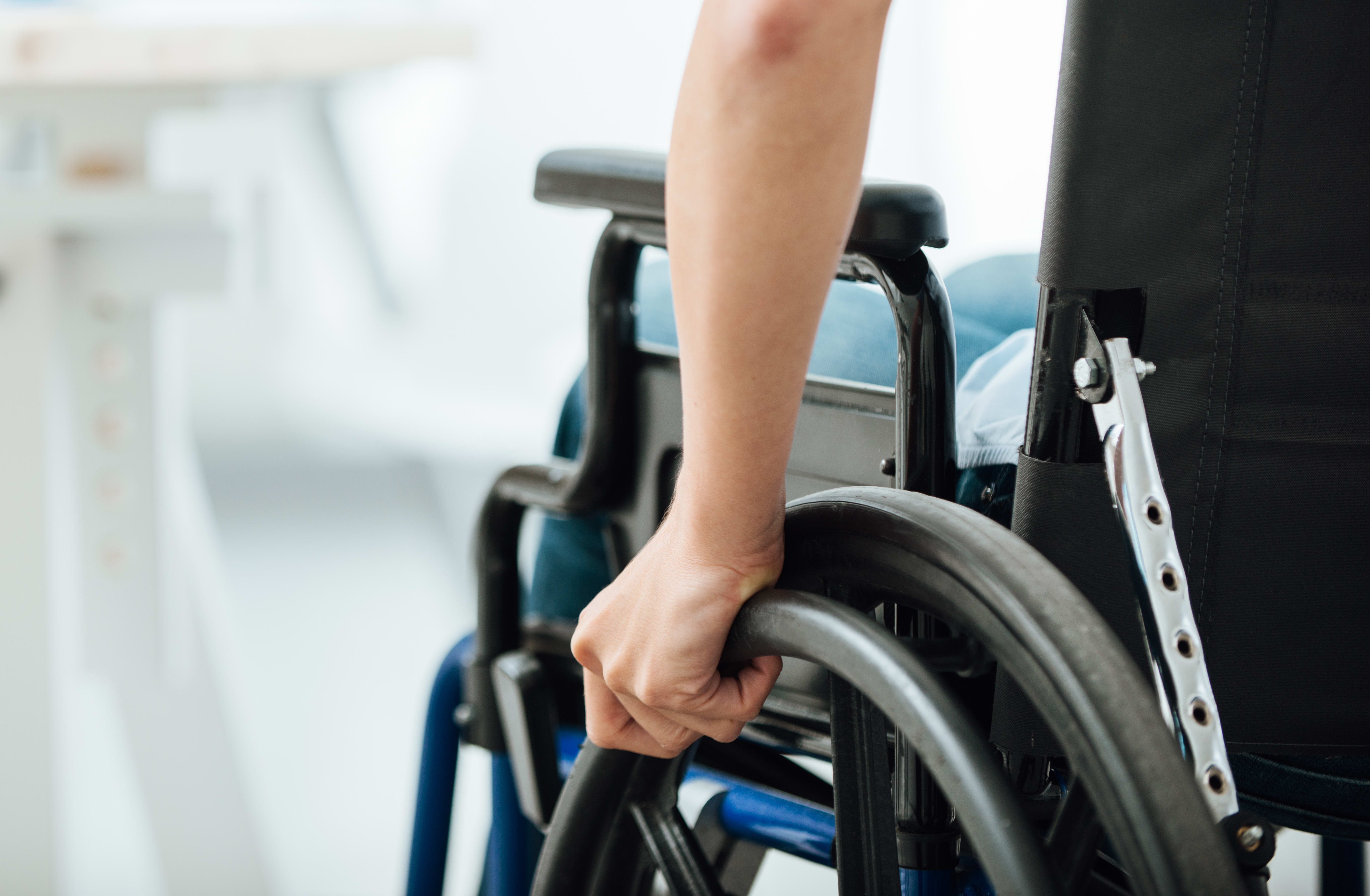 Woman in wheelchair next to an office desk, hand close up, unrecognizable person