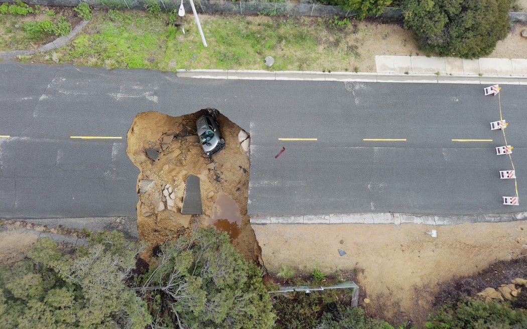 This aerial view shows two cars siting in a large sinkhole that opened during a day of relentless rain, January 10, 2023 in the Chatsworth neighborhood of Los Angeles, California. - A massive storm has arrived and is expected to cause widespread flooding throughout the state. (Photo by Robyn BECK / AFP)