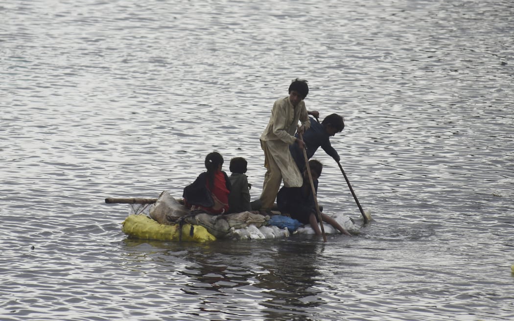 Children use a raft to make their way in a flooded area after heavy monsoon rains on the outskirts of Sukkur, Sindh province, on August 27, 2022. - Thousands of people living near flood-swollen rivers in Pakistan's north were ordered to evacuate on August 27 as the death toll from devastating monsoon rains neared 1,000 with no end in sight. (Photo by Asif HASSAN / AFP)