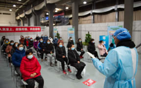 People listen as a staff member elaborates precautions before receiving Covid-19 vaccine shots at an inoculation site in Chaoyang District, Beijing, capital of China, Jan. 5, 2021.