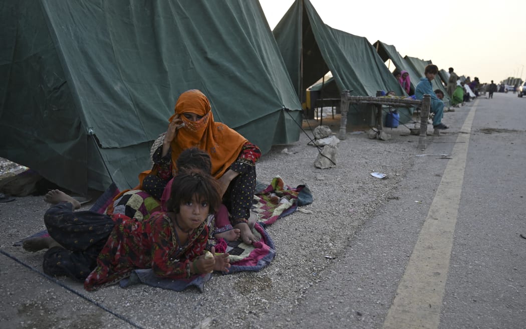 Internally displaced flood-affected people sit outside their tents at a makeshift camp after heavy monsoon rains in Sukkur, Sindh province on 5 September 5, 2022.