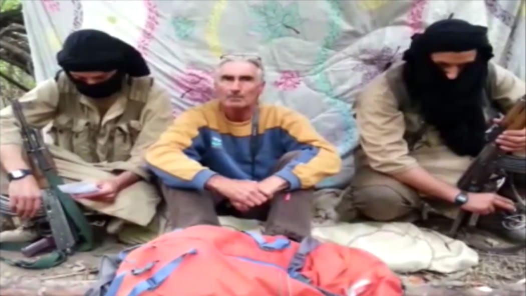An  image from a video released by Jund al-Khilifa on 22 September of  Herve Gourdel sitting between two armed jihadists at an undisclosed location.